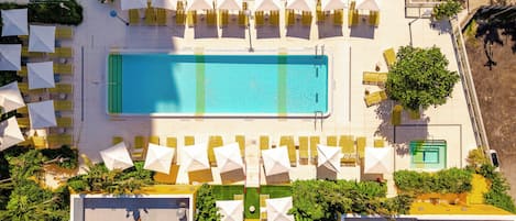 Ilmakuva hotellista, jossa on suuri uima-allas keskellä, useita oleskelualueita aurinkovarjoineen sekä vehreää kasvillisuutta ympärillä.