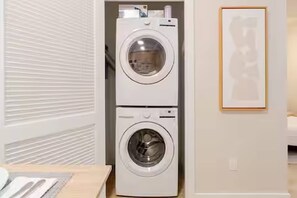 A laundry room with two stacked washing machines and a framed picture on the wall. - Unique Terrace in Midtown Pool (Miami)