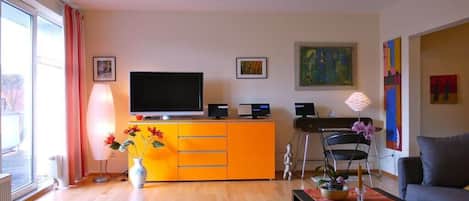 Un salon comprenant une télévision, un meuble jaune, une chaise, un canapé et une fenêtre avec des rideaux.