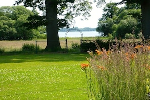 A grassy area with a metal archway leading to a body of water, surrounded by trees and a fence. - Holiday apartment with 1 bedroom (Bad Zwischenahn)