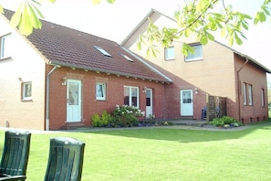 A two-story brick house with a sloped roof, a front porch, and a small garden area. - Holiday on the North Sea coast in Pilsum (Krummhörn Pilsum)