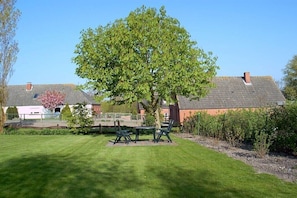 A well-maintained lawn with a picnic table and chairs, a large tree, and a building with a sloped roof in the background. - Holiday on the North Sea coast in Pilsum (Krummhörn Pilsum)
