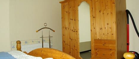 A bedroom with a wooden wardrobe, a bed with a blue and white bedspread, and a red vacuum cleaner.
