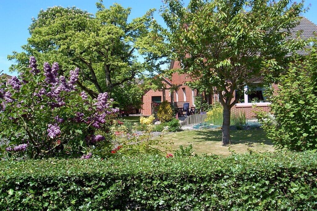 A residential garden with a brick house, a lawn, and various flowering plants.