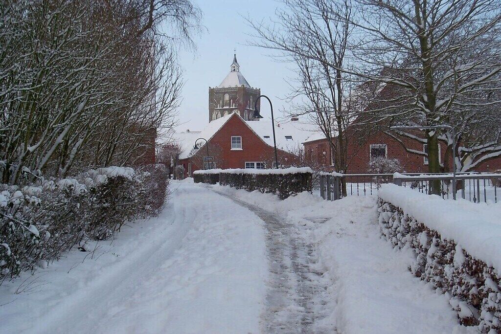 Eine verschneite Landstraße, die zu einer Kirche mit einem Glockenturm führt.