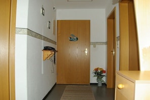 A hallway with a wooden door, a small shelf with a telephone, and a vase with flowers. - Holiday on the North Sea coast in Pilsum (Krummhörn Pilsum)