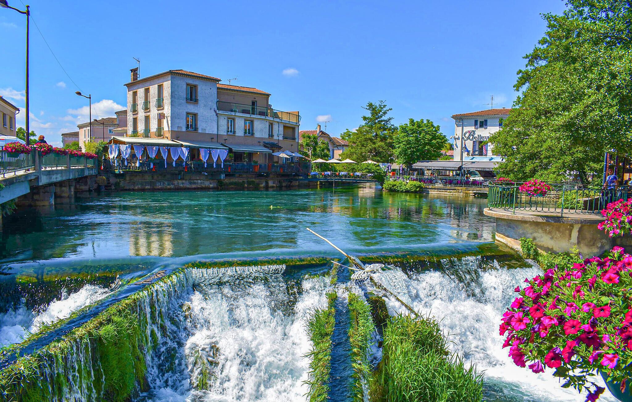 A riverside view with a bridge, buildings, and a waterfall.