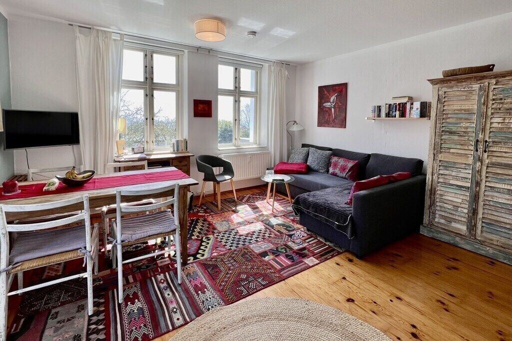 A furnished living room with a sofa, a dining table with chairs, a television, and a bookshelf.