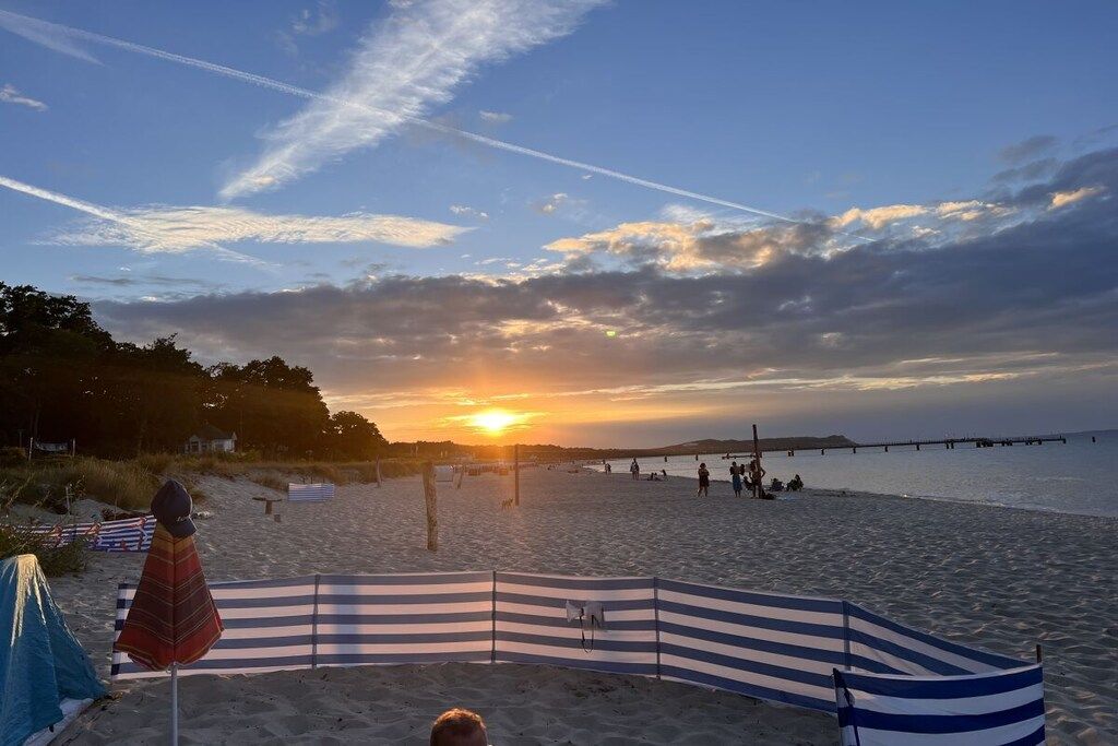 A beach with a sunset, a pier in the distance, and a striped beach umbrella.