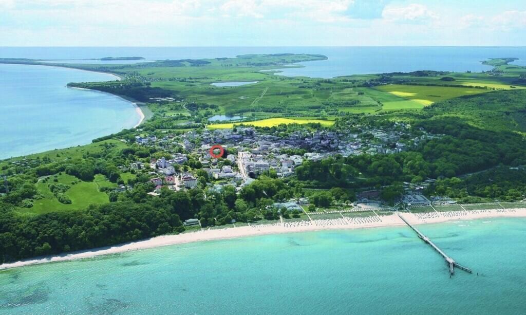 An aerial view of a coastal area with a beach, a pier, and a residential area with houses and greenery.