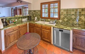 A kitchen with wooden cabinets, a green tiled backsplash, a stainless steel dishwasher, and a window with a view of greenery. - Cozy home in Besse sur Issole (Besse sur Issole)