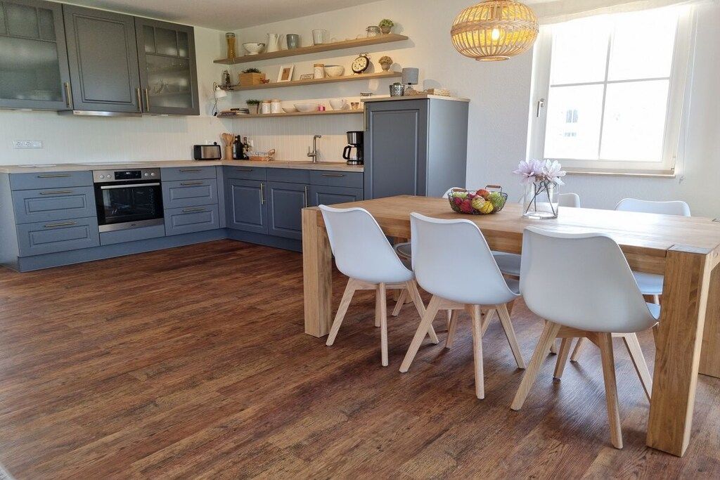 Una cucina moderna con mobili grigi, un tavolo da pranzo in legno e sedie bianche.