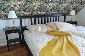 Ein Schlafzimmer mit einem Bett, zwei Nachttischen, einer Lampe auf jedem Tisch, einer Wand mit Blumenmuster und einem Holzboden.