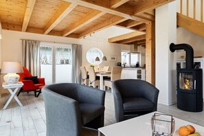 A modern living room with a fireplace, two grey armchairs, a dining table, and a kitchen area in the background. - Holiday home in Bohnert with sauna (Bohnert)