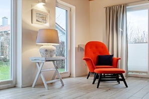 Una habitació amb una cadira moderna, un taulell amb una làmpada i una finestra amb cortines.