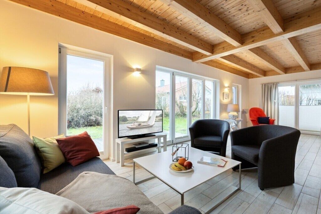 Ein modernes Wohnzimmer mit Fernseher, bequemen Sitzmöglichkeiten und großen Fenstern.
