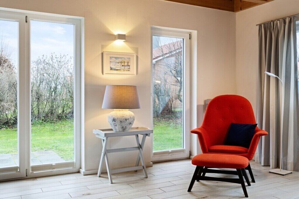 Een kamer met een rode stoel, een lamp op een bijzettafeltje en een ingelijste foto aan de muur.