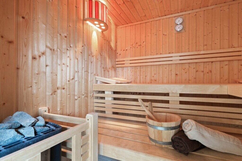 A wooden sauna with benches, a stone heater, a wooden bucket, and towels.