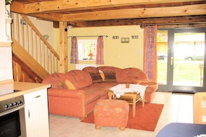 A cozy living room with a sofa, ottoman, and a small table with a candle. A wooden staircase leads to another room. - Nahnsen Farm, holiday under a thatched roof (Leck \/ Klintum)