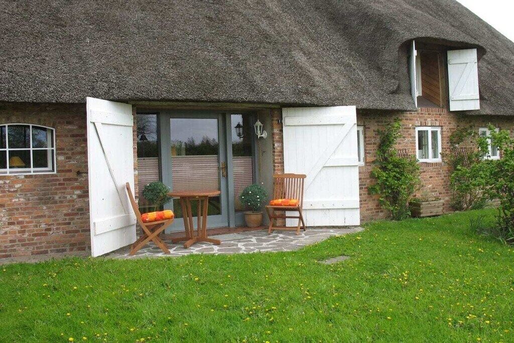 Ein reetgedecktes Cottage mit Backsteinfassade, einem Holztisch und -stühlen und einem kleinen Garten.