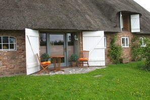 A thatched-roof cottage with a brick exterior, a wooden table and chairs, and a small garden. - Nahnsen Farm, holiday under a thatched roof (Leck \/ Klintum)