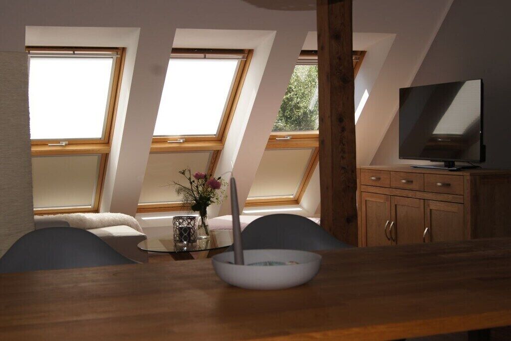 Een eethoek met een tafel, stoelen, een televisie en uitzicht door dakramen.