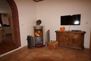 A living room with a wood-burning stove, a television mounted on the wall, and a wooden cabinet. - Holiday apartment with 2 bedrooms (Osteel)
