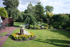 A well-maintained garden with a wooden deck, a stone planter with flowers, and a variety of trees and shrubs. - Holiday apartment with 2 bedrooms (Osteel)