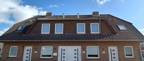 A two-story brick building with a tiled roof, a central entrance with a door, and a small window on the upper floor.