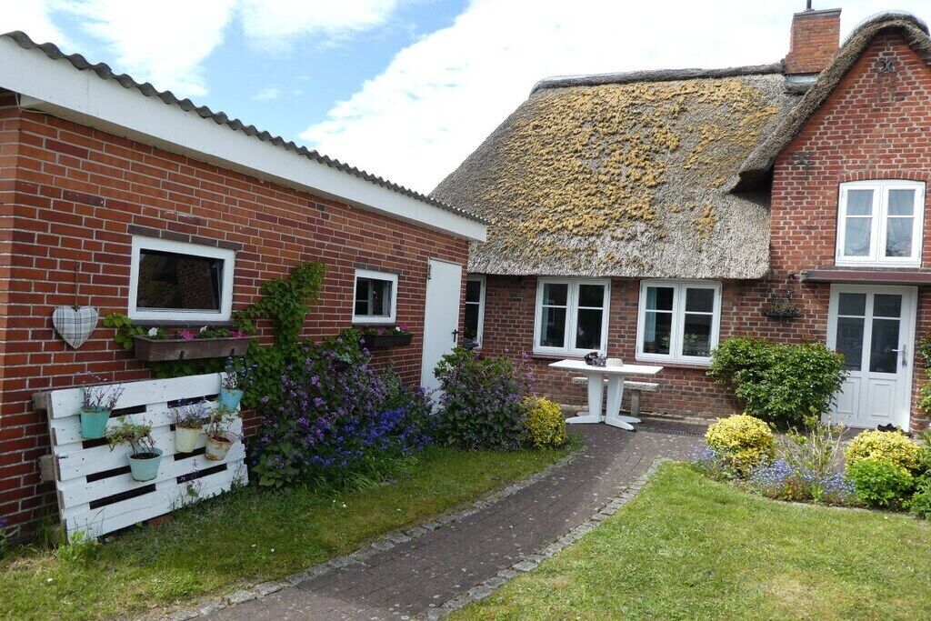A brick house with a thatched roof, a white picket fence, and a garden with various plants.