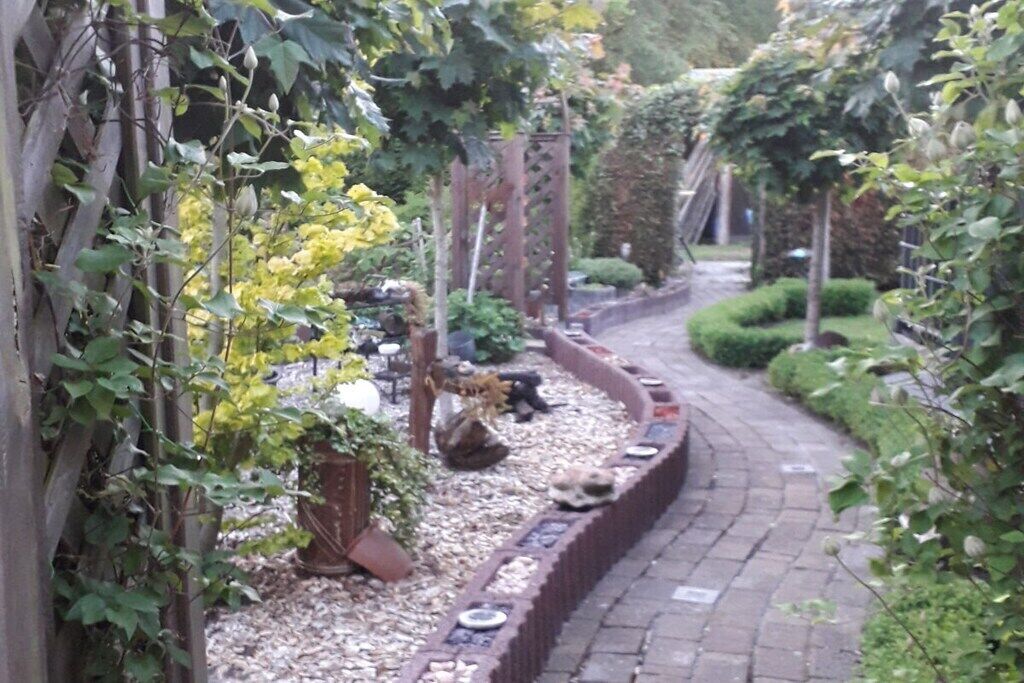 Ein Gartenweg mit gewölbter Backsteinrandung, umgeben von Grünpflanzen.