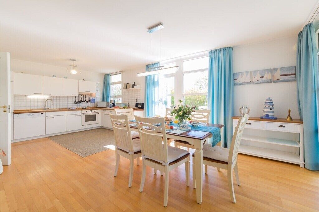 Une cuisine moderne avec des meubles blancs, une table à manger avec des chaises et une vue sur l’extérieur.