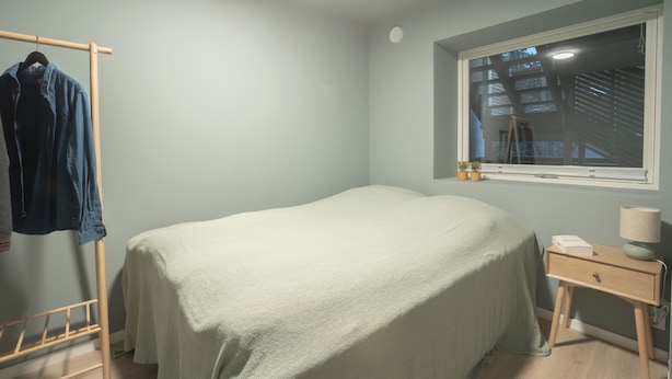 Un dormitorio con cama, mesita de noche con lámpara, ventana y perchero.