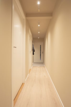 A corridor with a wooden floor, white walls, and doors on both sides. - Elegant and comfy apartment (Troms)