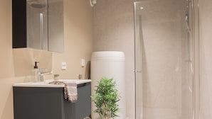 Un baño moderno con inodoro, lavamanos, espejo, ducha y una planta en maceta.
