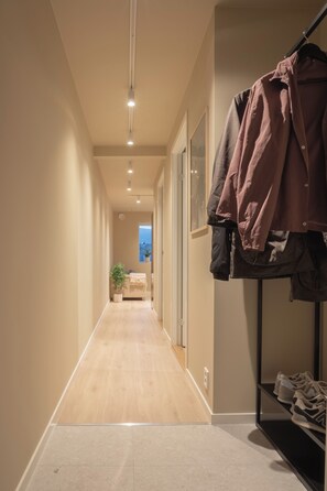 A hallway with a wooden floor, a coat rack with jackets, and a shoe rack with sneakers. - Elegant and comfy apartment (Troms)