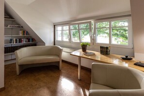 A room with a curved sofa, a wooden table with a plant, and a bookshelf. - Thatched holiday home (Bollingstedt)