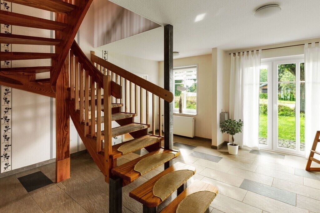 A wooden staircase with a modern interior design, leading to a room with a large window and a potted plant.