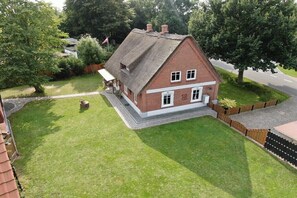 A two-story brick house with a thatched roof, surrounded by a well-maintained lawn and a wooden fence. - Thatched holiday home (Bollingstedt)