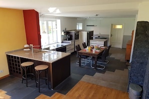 A modern kitchen with a central island, bar stools, a dining table, and a refrigerator. - Thatched holiday home (Bollingstedt)