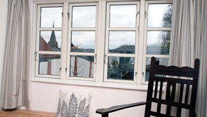 Ein Zimmer mit großem Fenster, einer hölzernen Bank und einem schwarzen Stuhl.