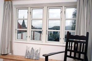 Ein Zimmer mit großem Fenster, einer hölzernen Bank und einem schwarzen Stuhl.