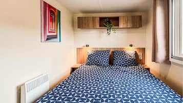Une chambre à coucher avec une couvre-lit à motifs, une tête de lit dotée d’un éclairage intégré, une œuvre d’art accrochée au mur et une fenêtre avec des rideaux.