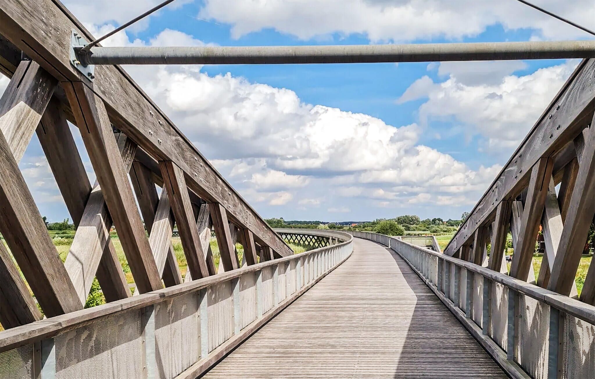 A wooden pedestrian bridge with a metal railing and a clear sky.
