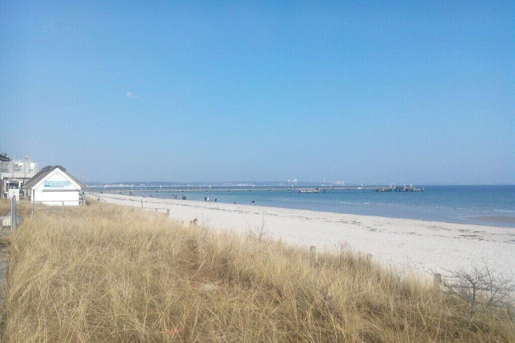 A beach with a building in the foreground, a clear sky, and a calm sea.