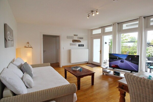 Ein Wohnzimmer mit einer Couch, einem Couchtisch, einem Fernseher und Blick durch große Fenster.