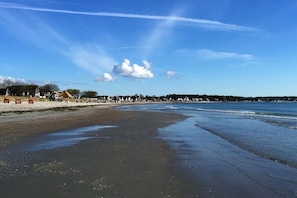 A beach with a clear sky, a sandy shore, and a distant shoreline with buildings. - Holiday home with 1 bedroom (Scharbeutz)