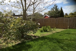 A fenced backyard with a grassy lawn, a wooden fence, and a tree. - Holiday home with 1 bedroom (Scharbeutz)