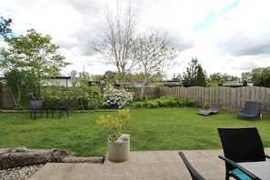 Ein Garten mit Rasen, einem Holzzaun und Gartenmöbeln, darunter Stühle und ein Tisch.
