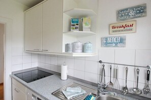 A kitchen with white cabinets, a stainless steel sink, and a hanging utensil rack. - Holiday home with 1 bedroom (Scharbeutz)